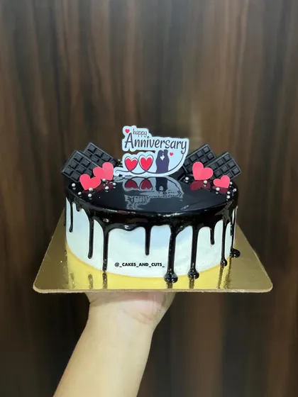 A delicious-looking chocolate drip anniversary cake, topped with chocolate bars and hearts.