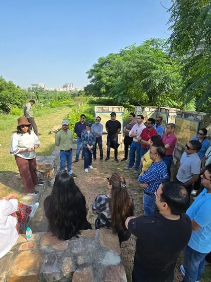 A group of corporate volunteers listens intently during a briefing at Ghata Bundh, learning about the land's history and its future as a public green space.