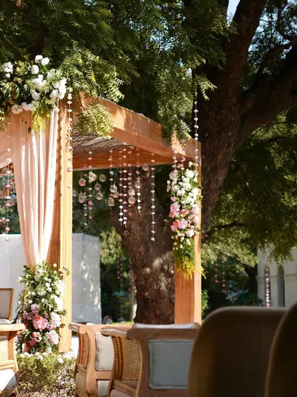 A closer look at the 'Bloom Grace' mandap, showing the delicate hanging floral strings and the beautiful arrangement of flowers on the wooden structure, all bathed in natural sunlight.