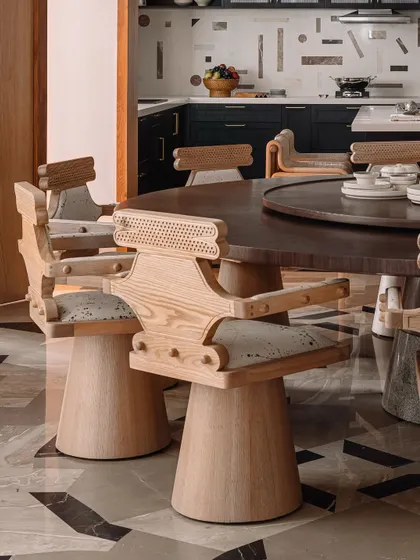 A close-up of the custom-designed dining chairs, showing the caned backrest and the unique, sculptural form of the ash wood frame.