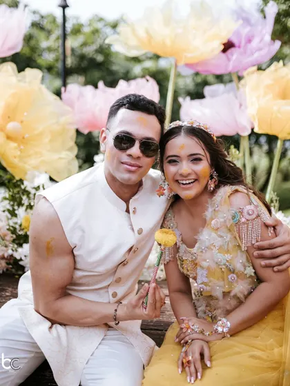 A sweet portrait of the couple amidst giant floral decorations at their Haldi, smiling and enjoying a quiet moment together.