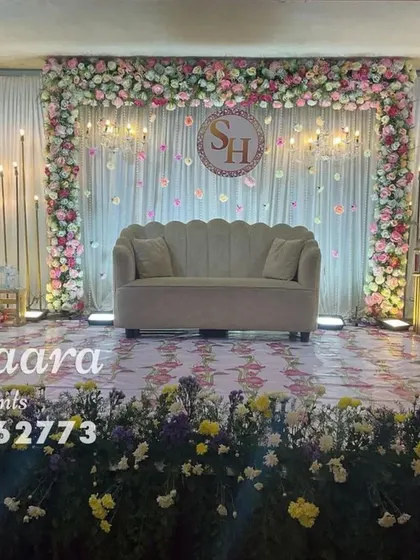 A beautiful stage design featuring a floral ring with a custom monogram, set against a backdrop of fairy lights. The hanging floral lanterns add a whimsical touch to this engagement or reception setup.