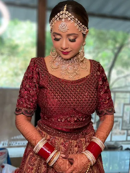 A classic Punjabi bridal look with a modern touch. The eyes are subtly defined, and the lips have a pop of color, all framed by a stunning matha patti.
