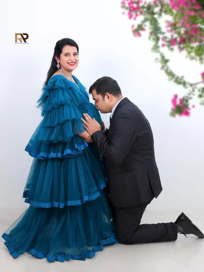 A formal and elegant couple's portrait. The dad-to-be is dressed in a suit, perfectly complementing his partner's stunning blue tiered gown.