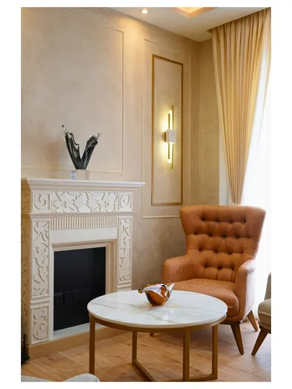 A cozy spot by a carved fireplace, featuring a classic tufted armchair in a warm tan leather, perfect for reading or relaxing.