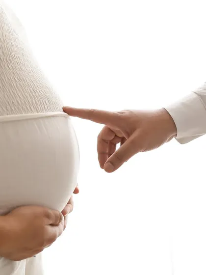 A playful and sweet close-up. The partner's finger gently touches the baby bump, a simple and tiny gesture that is full of meaning and love.