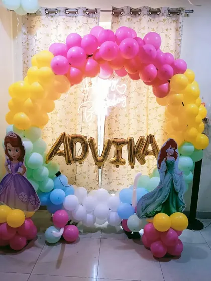 A princess-themed decoration for Advika's birthday at home. The colorful balloon arch is decorated with cutouts of her favorite Disney princesses.