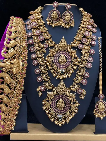 A heavy bridal set with intricate peacock and Lakshmi motifs, studded with red stones. This rental comes with a choker, long necklace, vaddanam, and maang tikka.