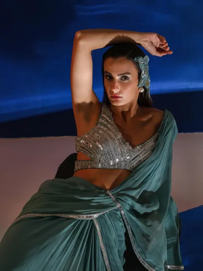 A modern take on ethnic wear, featuring a pre-draped saree with a heavily embellished blouse. The styling is enhanced by a statement headpiece, adding a touch of avant-garde elegance.