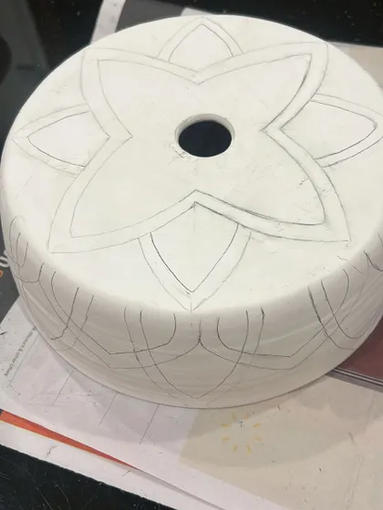 The journey of a lampshade begins with a pencil sketch on greenware (unfired clay). This is where the design is carefully planned before any carving or color is added.