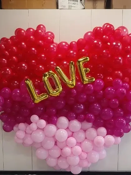A beautiful heart-shaped balloon wall made with three shades of pink and red. The "Love" foil balloon in the center makes it perfect for an anniversary or engagement party.