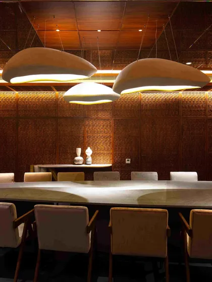 A close-up of the dining table and the pebble-like pendant lights from Design ni Dukaan. The organic shapes of the lights contrast beautifully with the geometric precision of the lattice work.