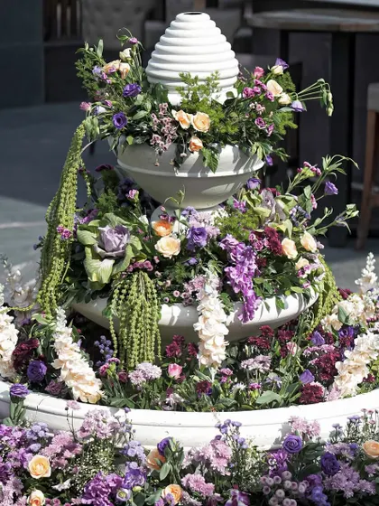 A tiered fountain overflowing with a beautiful mix of lilac, lavender, and peach florals, serving as a stunning centerpiece.