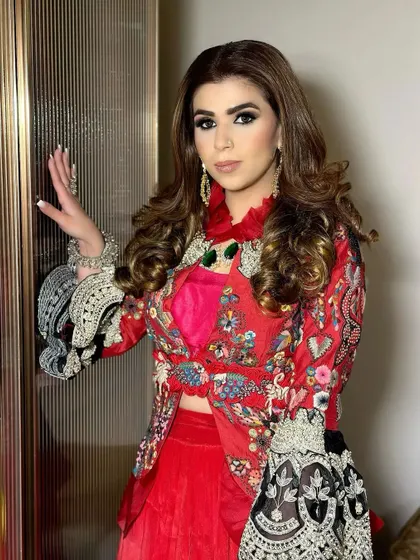 A client ready for a party in a stunning red embroidered outfit. Her hair is styled in large, bouncy curls, creating a look that is both festive and glamorous.