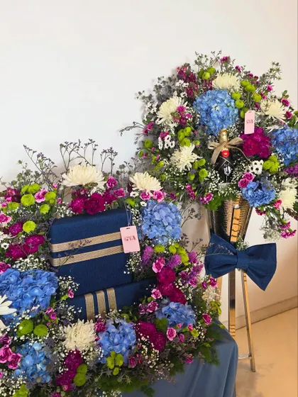This image shows the complete gift set, with a large floral arrangement on a stand and a coordinating gift tray filled with beautifully wrapped boxes and matching flowers.