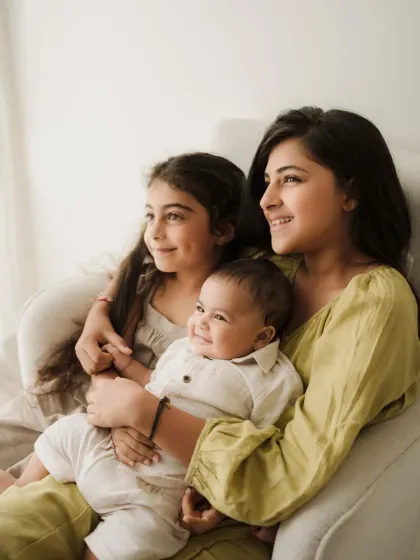 Three siblings sit together on a white armchair, sharing a happy moment. This photo showcases the beautiful bond between them.