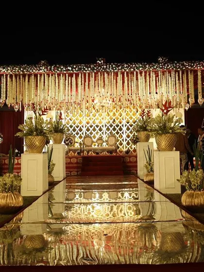 A mirrored aisle reflects the opulent decor, leading to a mandap adorned with traditional floral hangings and gold accents. This design creates a grand sense of arrival for the ceremony.