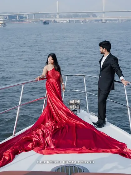 A powerful pose on the bow of a yacht, with the bride's long red trail gown spread out, creating a stunning visual against the water and the distant bridge.