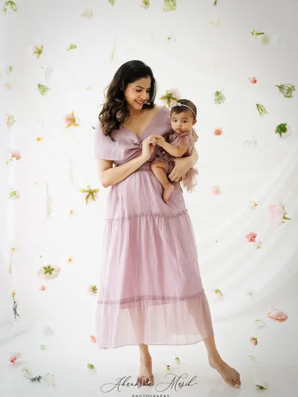 A mother holds her baby's hand in this sweet, full-length portrait. The floral background and soft colors add a touch of whimsy and romance.