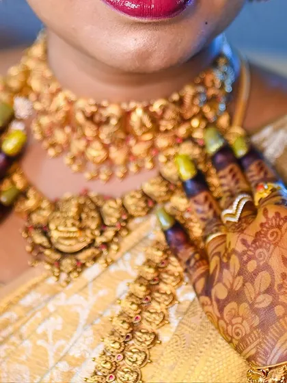 A close-up of the bride's hands near her traditional gold necklace, highlighting the deep color of the henna.