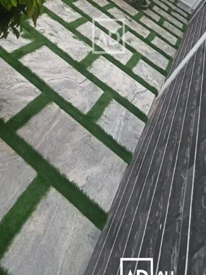 This image shows a combination of materials: a stone-paved path with artificial grass grouting next to a wall with dark cladding.