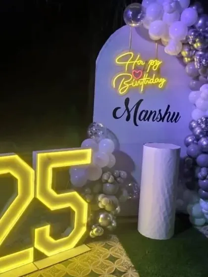 A 25th birthday celebration at night with a purple and silver balloon arch and a large '25' marquee light.