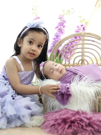 A beautiful portrait of sisterhood. The older sister looks on, ready to be a guide and friend, while her newborn sister sleeps peacefully in a floral setting.