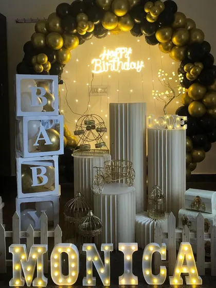 This black and gold birthday package includes the full set of props for a complete look. It features the balloon ring, neon sign, 'BABY' display boxes, a picket fence, and marquee letters.