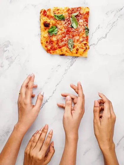A conceptual flatlay with a single slice of pizza and multiple hands reaching for it. This artistic shot plays with minimalism and desire, perfect for a creative ad campaign.