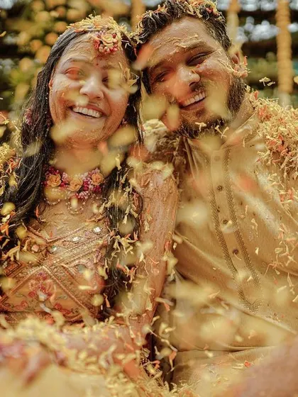 A beautiful shot of the couple covered in flower petals, smiling at the end of their Haldi ceremony.