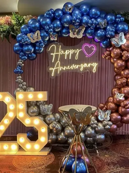 A 25th-anniversary celebration with a circular balloon arch in blue, silver, and rose gold, accented with butterflies and marquee numbers.