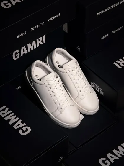 A clean, high-end shot of white leather sneakers surrounded by branded boxes. The dark, moody lighting and sharp focus convey a sense of premium quality and exclusivity for a feature product page.