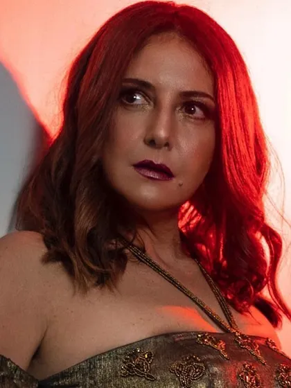 A close-up beauty shot with dramatic red lighting. The makeup features a bold, vampy lip and smokey eyes, creating an intense and captivating look.
