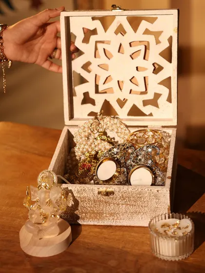 A beautiful white-washed wooden box filled with festive goodies for Diwali. This hamper includes decorative candles and pearl garlands.