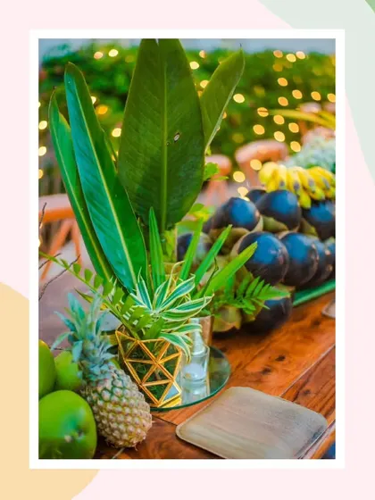 A detail of the table centerpiece, where tropical leaves and locally sourced fruits are arranged in a modern gold-plated vase, blending rustic charm with a touch of contemporary elegance.