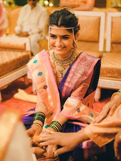 A beautiful moment from a Marathi wedding ceremony where the bride participates in a ritual with her parents. Her happy and serene expression shows the importance of family blessings.