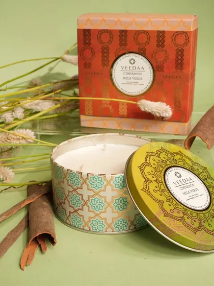 Our Cinnamon Mela Verde candle in its decorative tin, surrounded by cinnamon sticks. This fragrance is a warm and spicy blend, perfect for creating a cozy, festive feeling in your home.