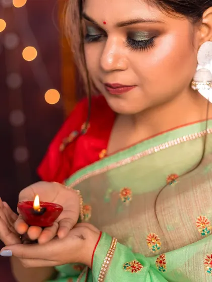A close-up shot focusing on the model's expressive look and the glowing diya. This image is rich with festive detail, from the makeup to the traditional clothing.