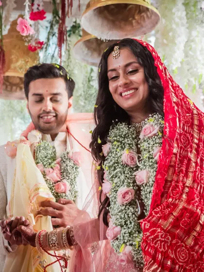 A beautiful moment from the wedding ceremony. The couple, adorned with floral garlands, smiles during a ritual, their bond evident.