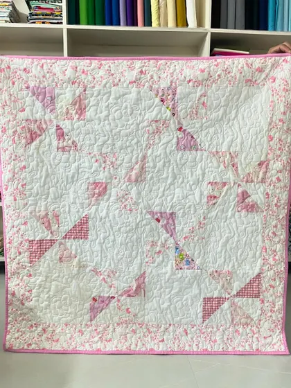 A delicate baby quilt in shades of pink and white. The pinwheel block pattern and floral border create a soft and gentle look for a nursery.