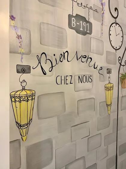 "Bienvenue Chez Nous" or "Welcome to our home." This hand-lettered phrase, along with vintage-style lanterns, adds an authentic French touch to the entryway mural.