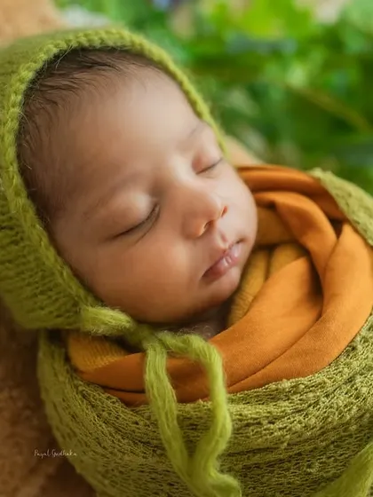 A sleeping newborn, swaddled in earthy green and orange tones. The textures of the knit wrap and bonnet add to the cozy, natural feel of this Boho-inspired shot.