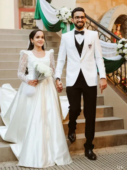 Ryan and Ela descending the church steps, hand in hand. The groom's sharp white tuxedo and the bride's classic gown with a long train created a picture of timeless elegance.