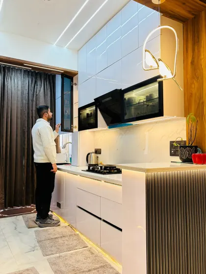 Inspecting the final details of a white modular kitchen. This design features high-gloss white cabinets, a built-in chimney, and a breakfast counter with a fluted panel base, combining style and practicality.