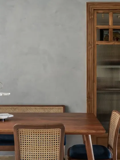 The dining area in 'Malhar' is defined by its custom wood and fluted glass doors, which lead to the puja room. The space is a blend of modern design and traditional elements.