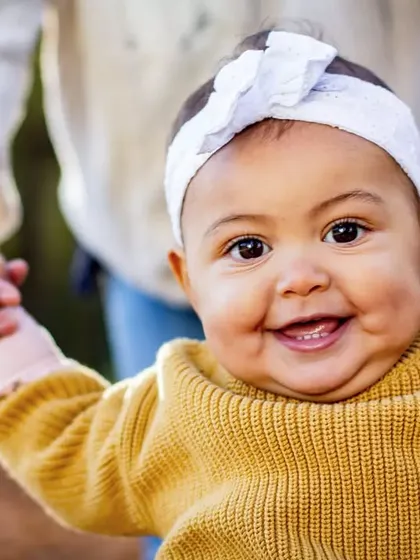 That big, gummy smile is just the best. This close-up captures the pure happiness of a baby who is learning to stand with a little help.
