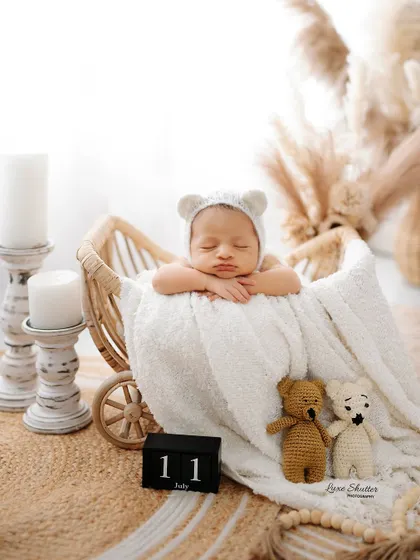 A beautiful shot of a newborn with a bear-ear bonnet, resting peacefully in a rustic basket. The neutral color palette and soft textures make this a classic newborn photo.
