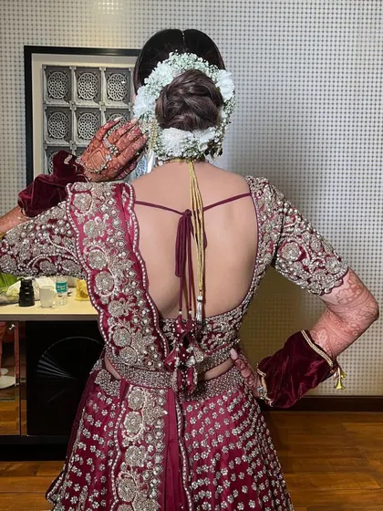 A back view of a bridal updo for a bride in a rich maroon lehenga. The bun is neatly wrapped with a gajra of fresh white flowers, creating a beautiful contrast and a classic wedding look.