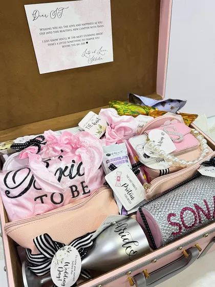 A peek inside a fully loaded bridal trunk. This hamper is packed with personalized items like a "Bride to be" sash, a custom tumbler, pouches, and a heartfelt note.