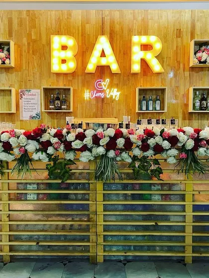 This rustic wooden bar was decorated with lush bouquets of red and white roses for a wedding reception. The setup includes our light-up "BAR" sign and custom branding with the #CheersValley neon sign.